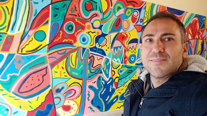 Rosario Annunziata in the Studio: Il murales è stato realizzato in collaborazione con istituzioni pubbliche per promuovere l'inclusione . Si vede il dettaglio della stampa sulla t-shirt